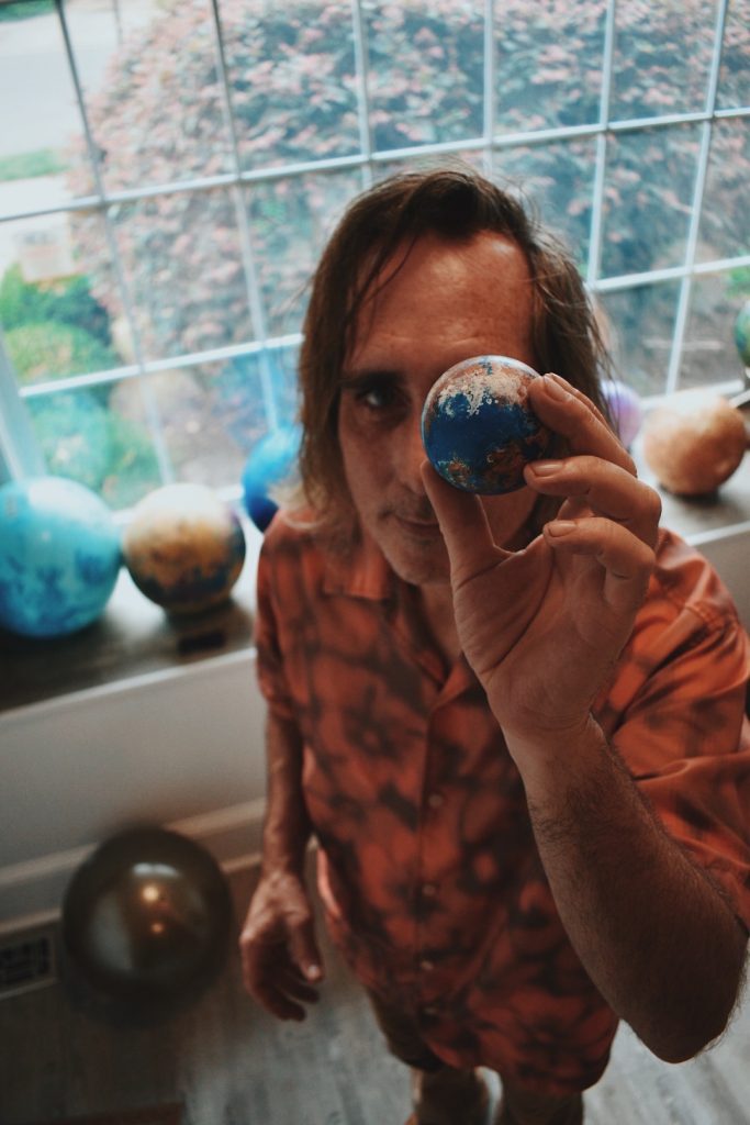 Wayne holding up globe with background of larger world globes